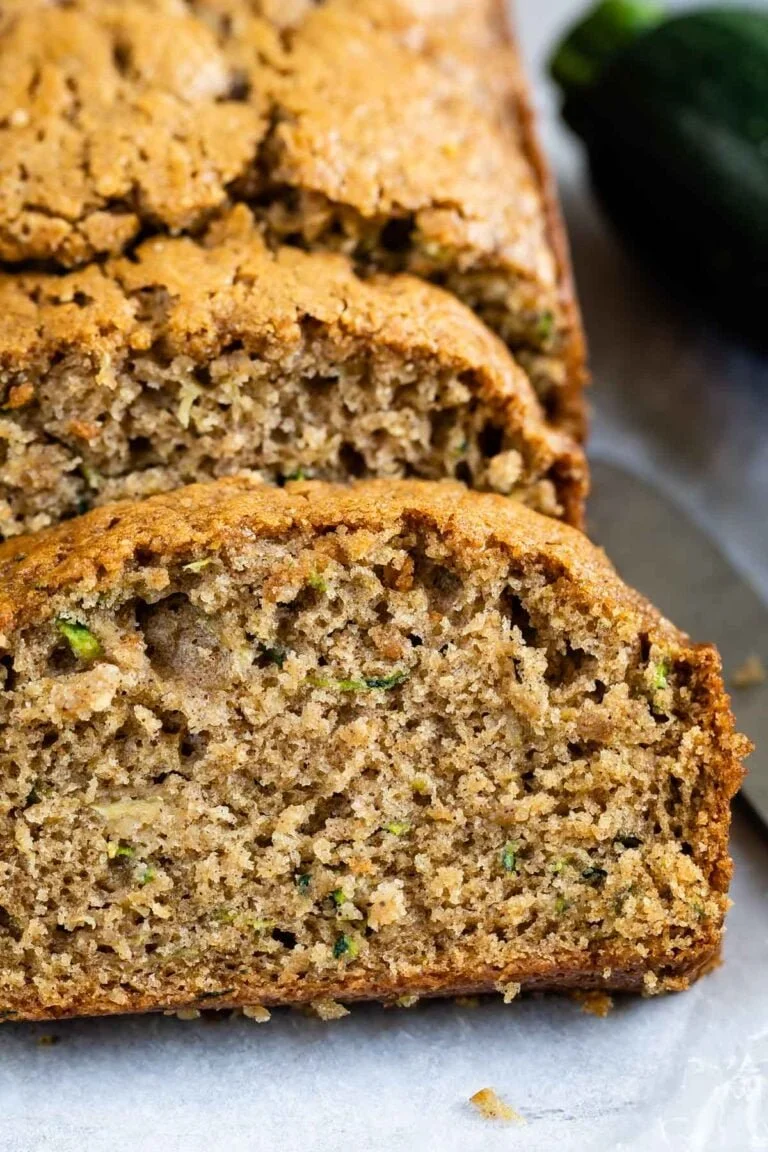 Freshly baked zucchini bread loaf with slices on a wooden cutting board.