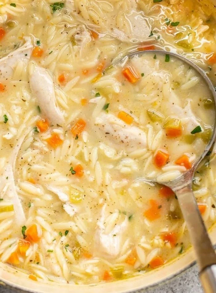 A bowl of Lemon Chicken Orzo Soup garnished with herbs and lemon slices.