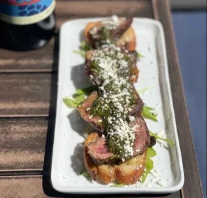 Delicious steak crostini topped with fresh herbs and cheese on a wooden board