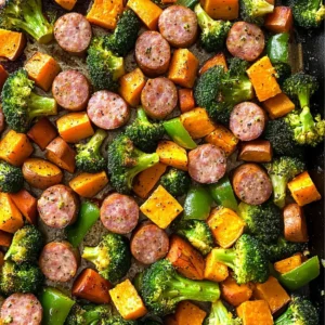 Sheet pan containing sausage and assorted colorful veggies ready to bake.